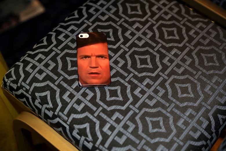 An iPhone whose case is covered by a photo of Tucker Carlson's face, resting on a conference room chair.
